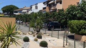 Een woonwijk met een rij huizen, een verharde weg en een aangelegde tuin met cactussen en struiken.