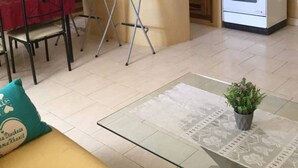 Cocina compacta con armarios de madera, estufa a gas, refrigerador y un pequeño comedor con una mesa roja y dos sillas.