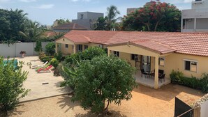Un barrio residencial con una casa de techo con tejas rojas, una piscina y un patio con mobiliario exterior.