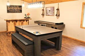 A billiards table with a wooden bench, a bar area with a sign, and wall-mounted lights.