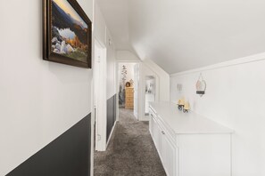 A hallway with a painting, a white dresser, and a small table with decorative items.
