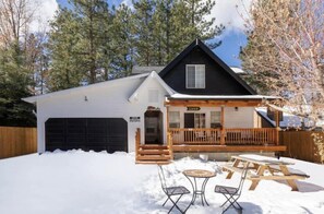A cabin with a covered porch, a garage, and a snow-covered yard with picnic tables.