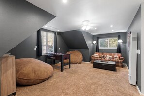 Une pièce de style loft avec un plafond haut, une table de baby-foot, un canapé et une fenêtre avec des stores.