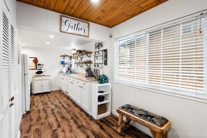 A kitchen with white cabinets, a wooden floor, a coffee bar, and a sign that says 'Gather'.