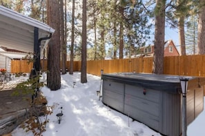 A backyard with a wooden fence, tall trees, and a hot tub.