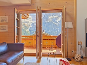 Un interior de madera con un sofá de cuero, una mesa con lámpara y vistas a montañas a través de puertas abiertas.