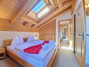 A wooden room with a skylight, a bed with pillows, a nightstand, and a wooden wardrobe.
