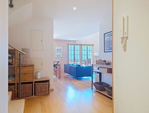 A spacious hallway with a dining area, a kitchen, and a living room with a blue sofa.