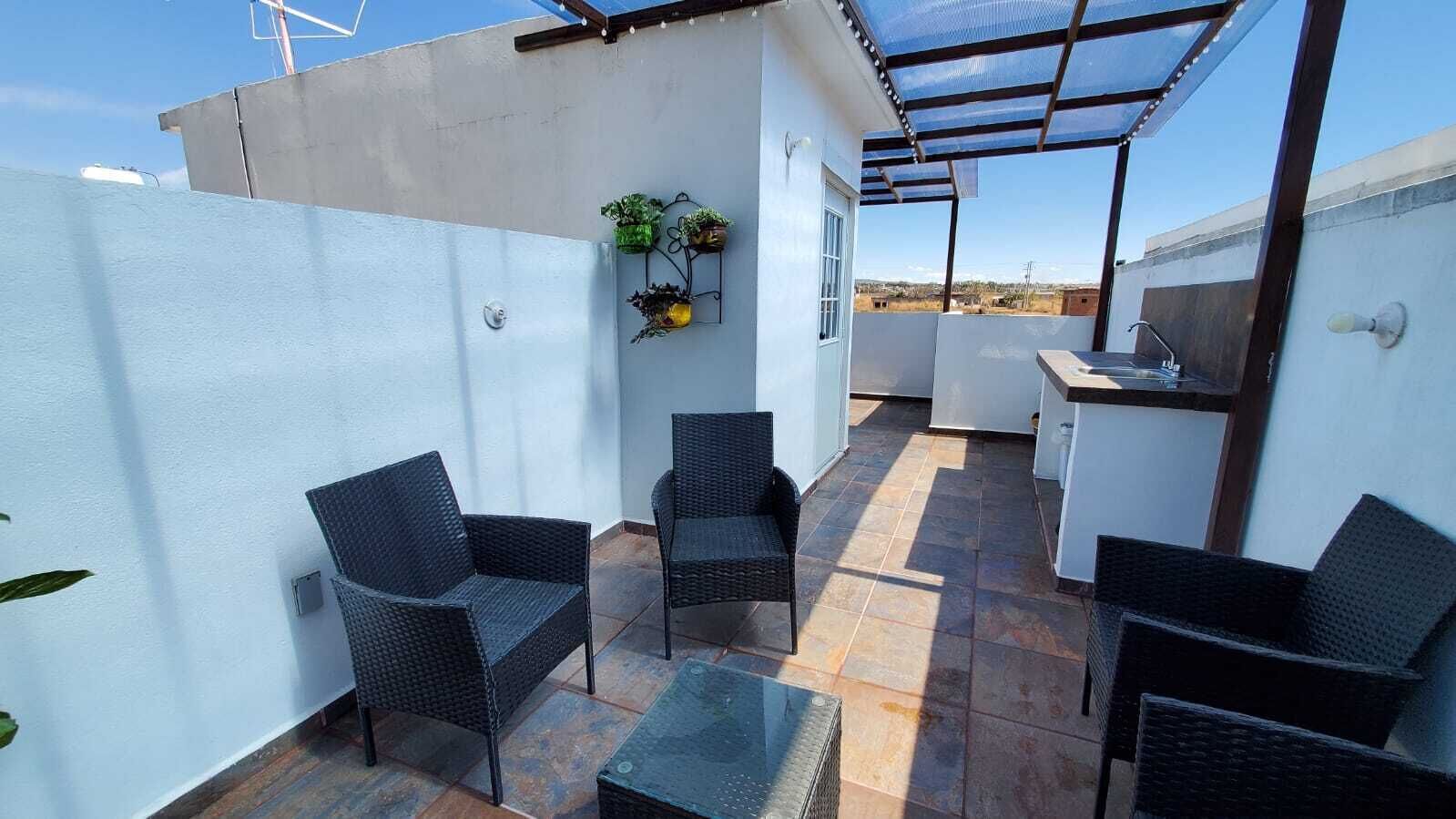 A rooftop patio with wicker furniture, a small table, and a kitchen area.