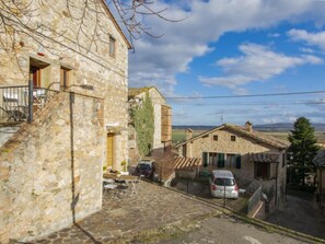 A stone building with a balcony, a small table with chairs, and a car parked in front. - Casa Francesca by Interhome (Sovicille)