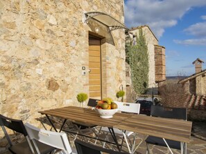An outdoor seating area with a stone wall, a wooden table, and chairs. - Casa Francesca by Interhome (Sovicille)