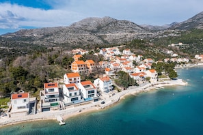 A coastal town with buildings along the waterfront, a clear blue sea, and mountains in the background.