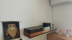 Een kamer met een houten kast, een flatscreen televisie op een houten plank, een wandairconditioning en een oliefoto van een uil.