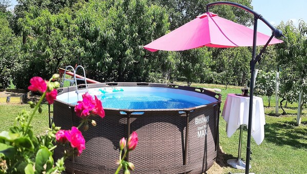 An outdoor swimming pool with a metal frame and a pink umbrella.