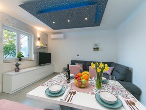 Una cocina moderna con una mesa de comedor dispuesta para cuatro personas, una televisión y un sofá al fondo.
