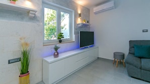 Ein modernes Wohnzimmer mit Fernseher auf einem weißen Schrank, einem grauen Sofa und einem kleinen Hocker.