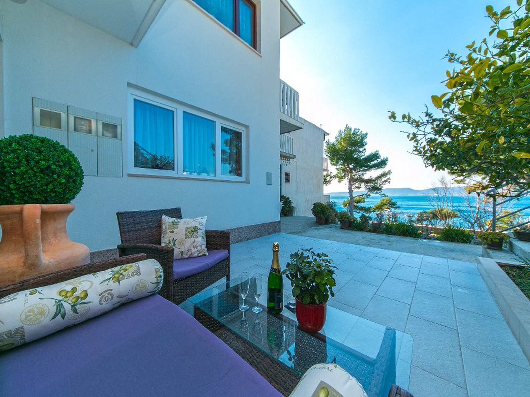 A modern outdoor seating area with a glass table, cushions, and a bottle of champagne.