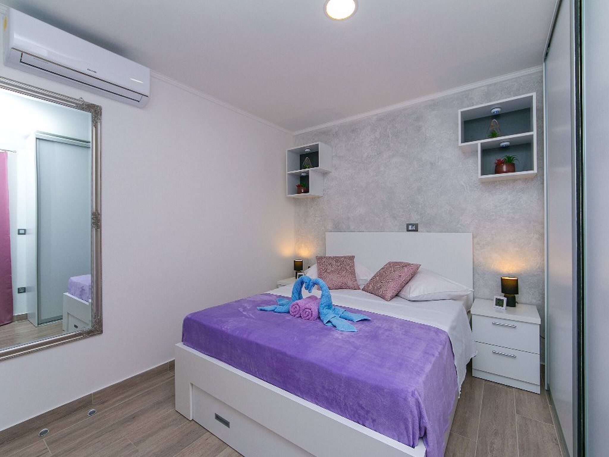 Um quarto moderno com uma cama grande, abajures, um espelho e prateleiras embutidas.
