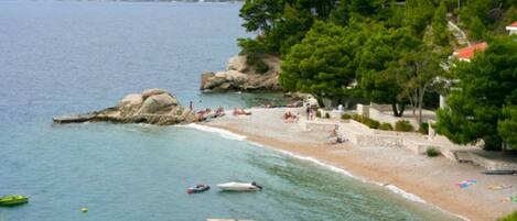 A coastal beach with boats, a stone wall, and trees.