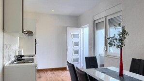 Eine moderne Küche mit weißen Schränken und Holzboden, die in einen Essbereich mit weißem Tisch und schwarzen Stühlen übergeht.