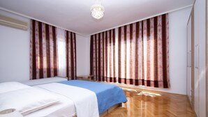 A hotel room with two beds, wooden flooring, a chandelier, and patterned curtains.