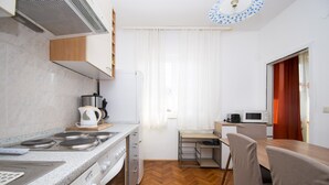 A compact kitchen with a stove, microwave, and sink, a dining area with a table and chairs, and a window with curtains.