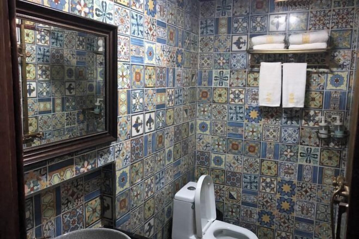 A bathroom with a tiled wall, a toilet, a sink, and a mirror.