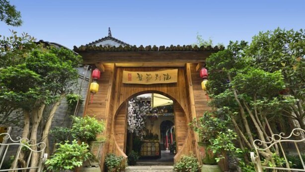 A traditional wooden archway entrance with a sign, surrounded by potted plants and a stone pathway. - Fanhua Courtyard (Chongqing)