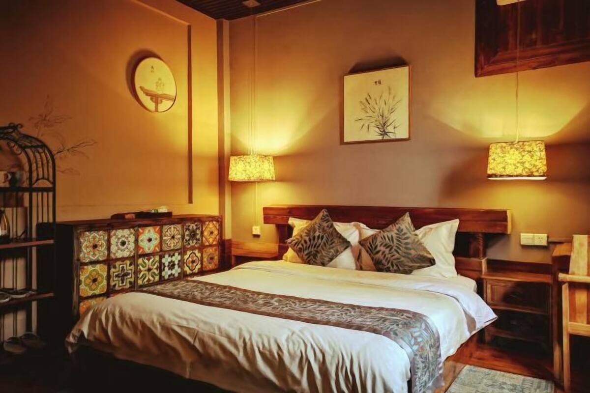 A bedroom with a large bed, patterned headboard, two bedside lamps, and a wall-mounted artwork.
