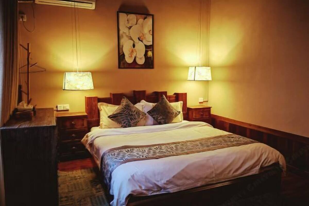 A hotel room with a large bed, two bedside lamps, a nightstand, a wooden headboard, and a framed artwork on the wall.
