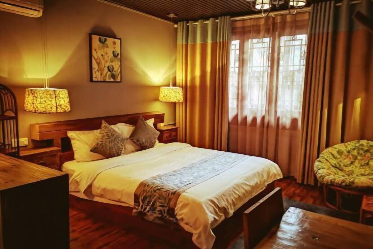 A hotel room with a large bed, two bedside lamps, a wooden headboard, a green chair, and a window with curtains.