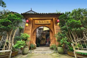 A traditional wooden archway entrance with a sign, surrounded by potted plants and trees. - Fanhua Courtyard (Chongqing)