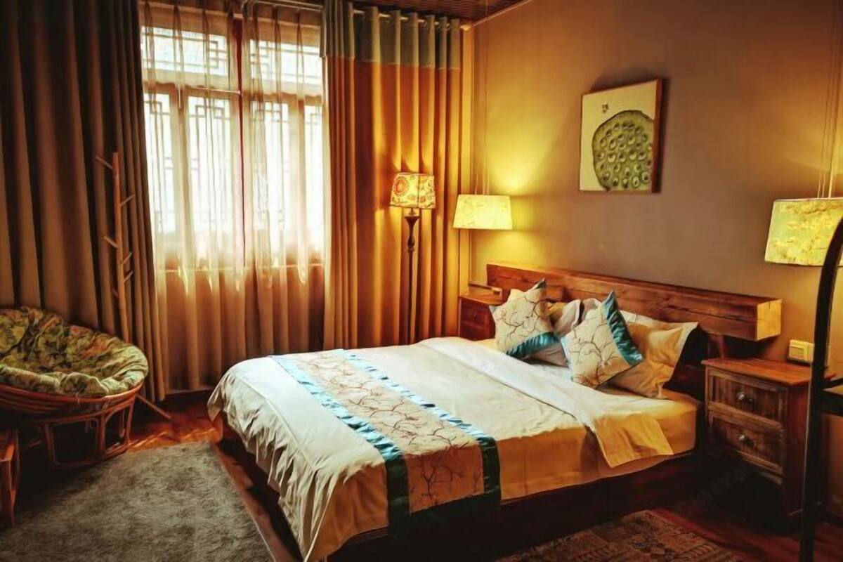 A neatly arranged bedroom with a bed, bedside lamps, a chair, and a wall-mounted artwork.