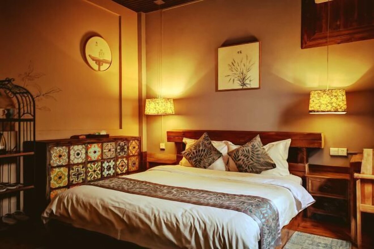 A neatly arranged bedroom with a large bed, two bedside lamps, a wooden headboard, and a decorative cabinet.
