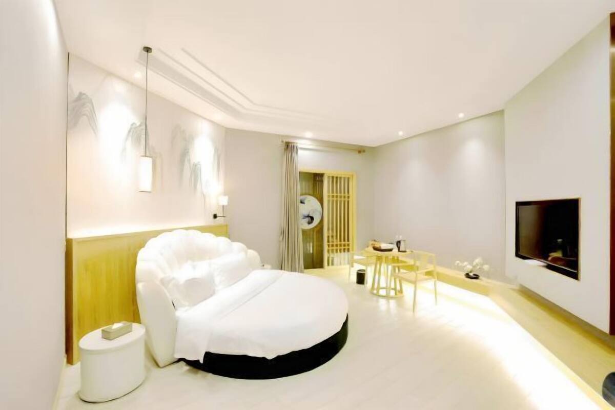 Una habitación de hotel moderna con una cama grande, un televisor, una mesita y una silla.