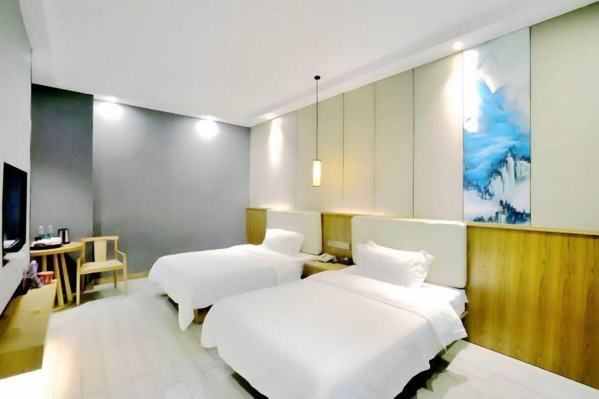 Habitación de hotel con dos camas, un escritorio con silla, un televisor y un cuadro en la pared.