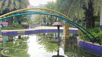 A water feature with a curved bridge, surrounded by palm trees and a tiled walkway.