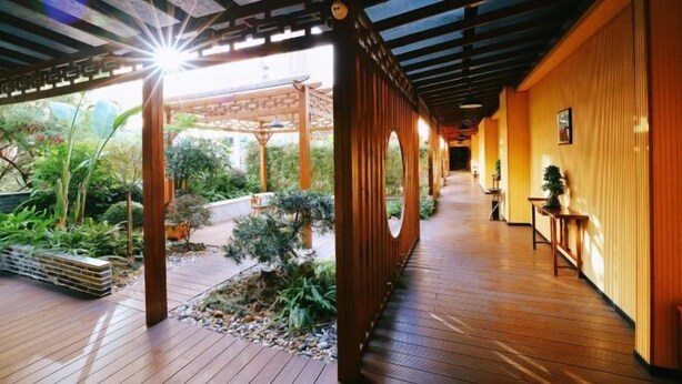 A wooden corridor with a covered outdoor area, wooden walls, and a small table with a plant. - Haolilai Garden Hotel (Sanming)