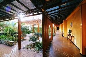 A wooden corridor with a covered outdoor area, wooden walls, and a small table with a plant. - Haolilai Garden Hotel (Sanming)