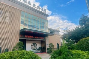 A modern building with a large glass facade, a prominent entrance with a red sign, and a landscaped area with greenery. - Haolilai Garden Hotel (Sanming)