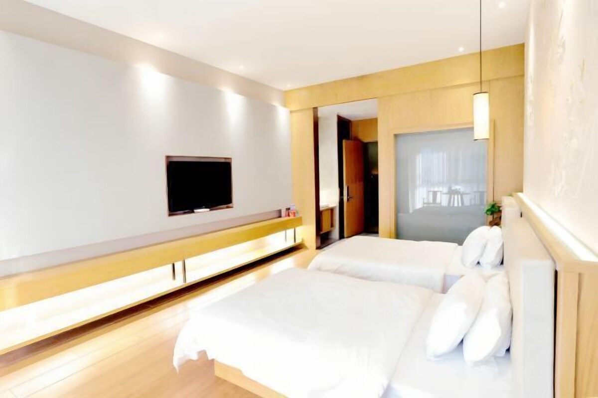 A modern hotel room with a large bed, a TV mounted on the wall, and a wooden bench.
