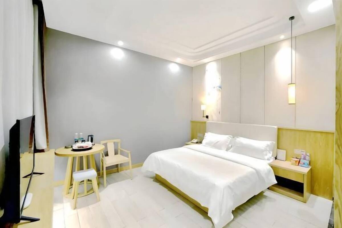 Habitación de hotel con cama, mesita de noche, silla, televisor y una pequeña mesa con lámpara.