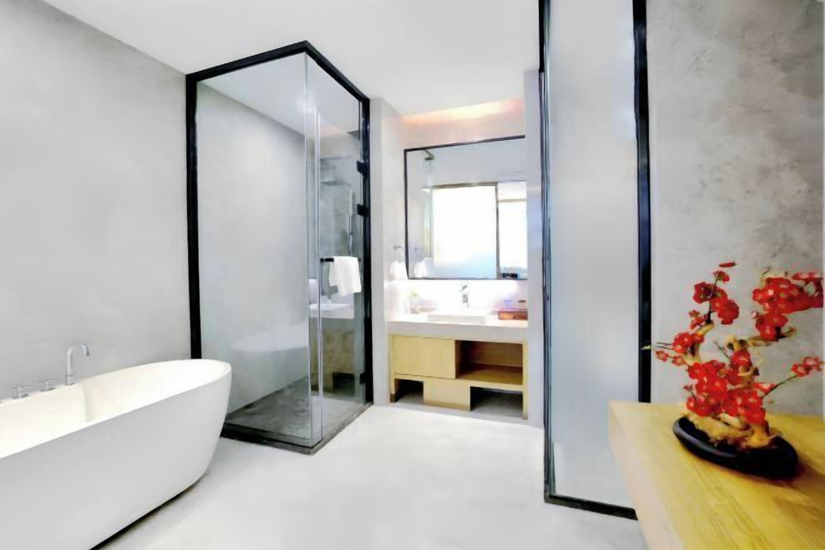 A modern bathroom with a freestanding bathtub, a glass shower enclosure, and a wooden vanity with a vase of red flowers.