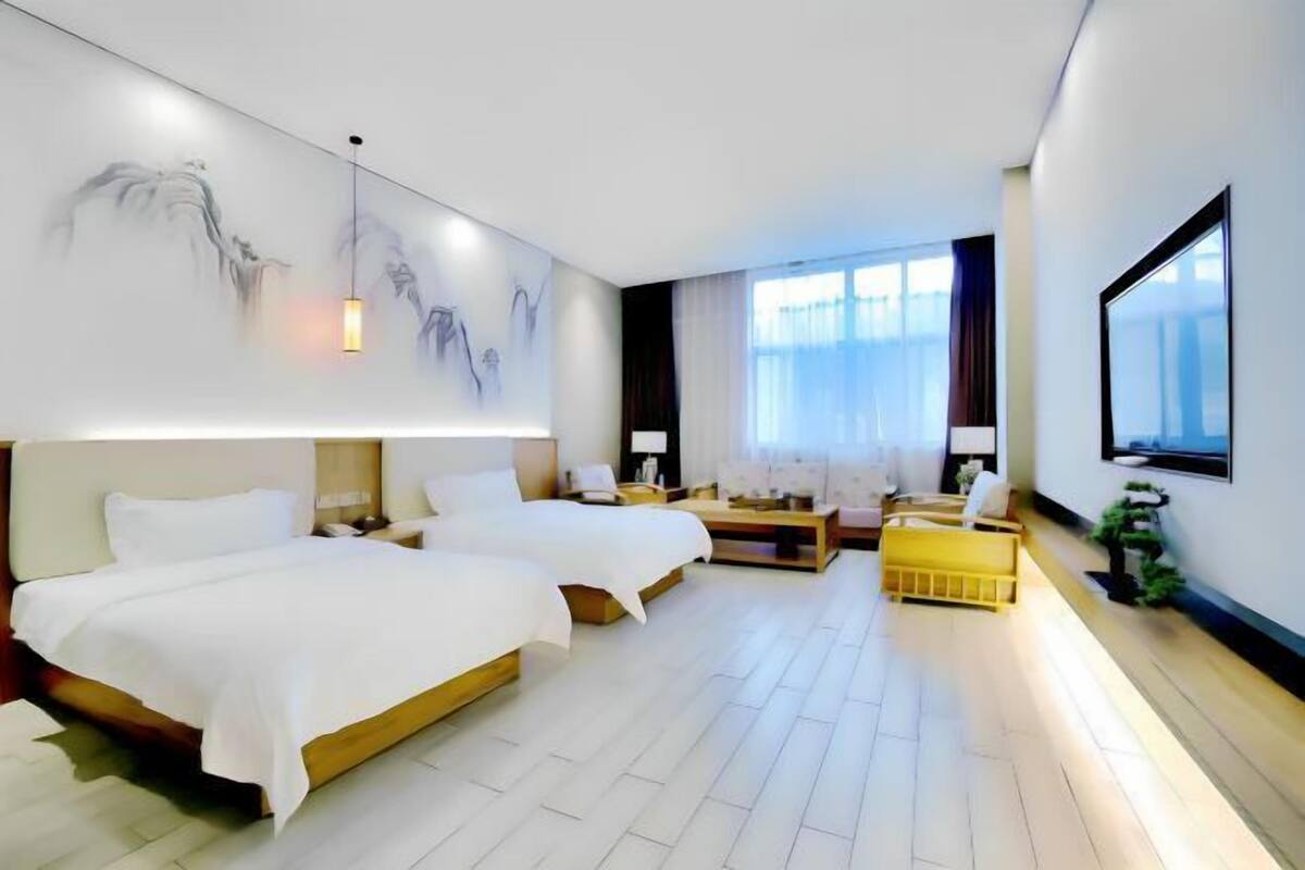 Habitación de hotel con dos camas, un escritorio, una silla, un sofá, un televisor y obras de arte en las paredes.