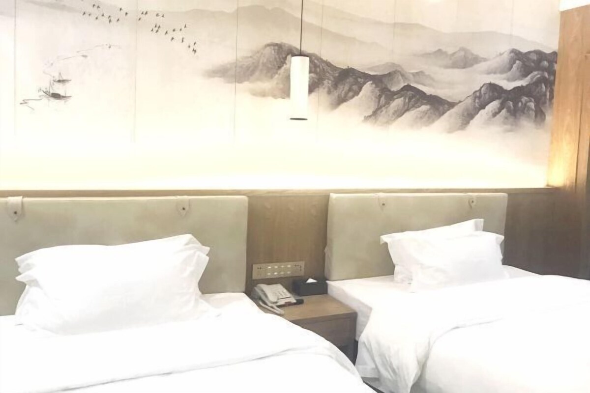 A hotel room with two beds, a wooden headboard, a wall-mounted telephone, and a painting of mountains.