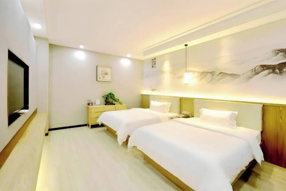 Habitación de hotel con dos camas, televisión, mesita de noche y una obra de arte en la pared.