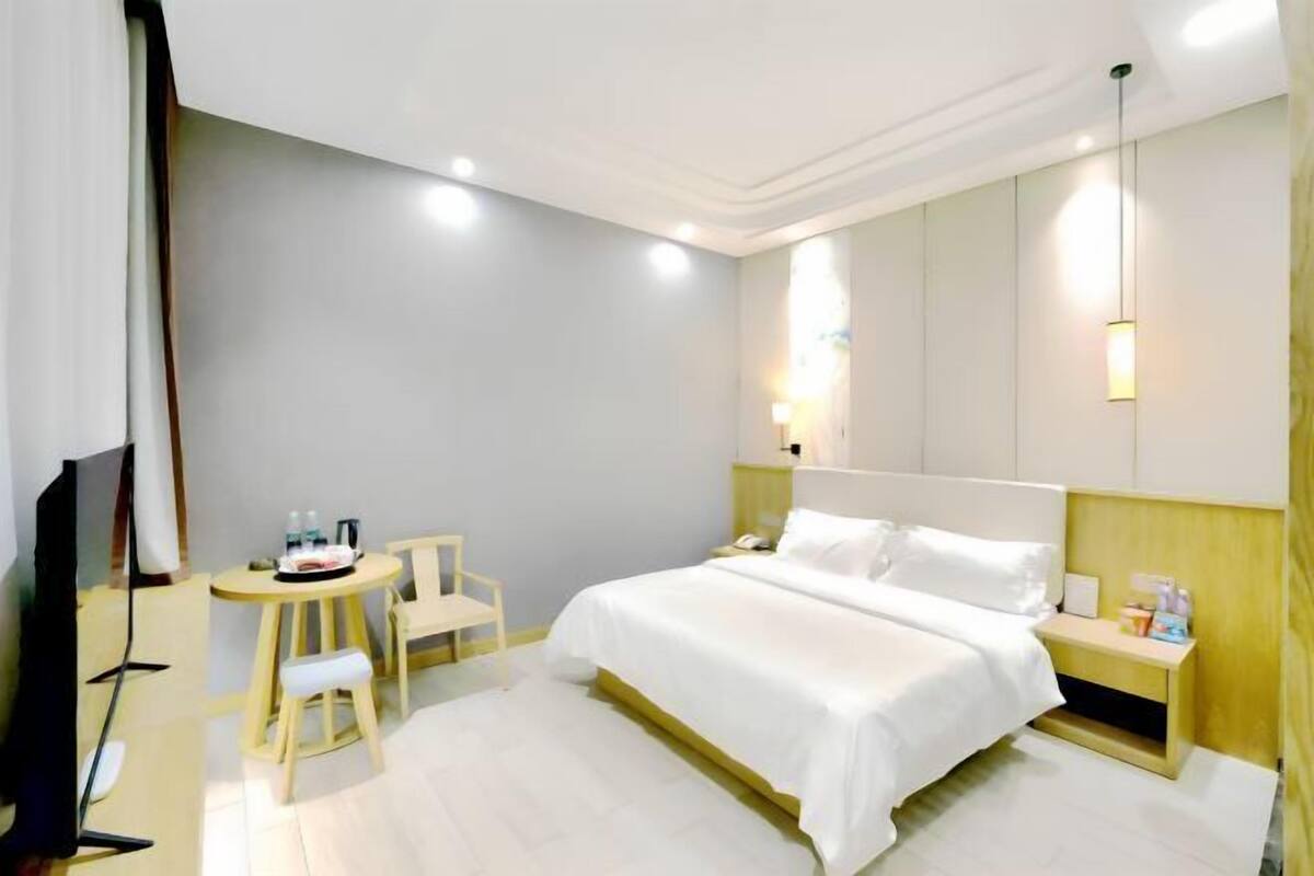 Una habitación de hotel con cama, mesita de noche, silla, televisor y una pequeña mesa con objetos encima.