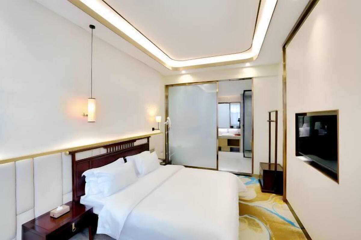 Una habitación de hotel con una cama grande, mesitas de noche, un televisor y un espejo.
