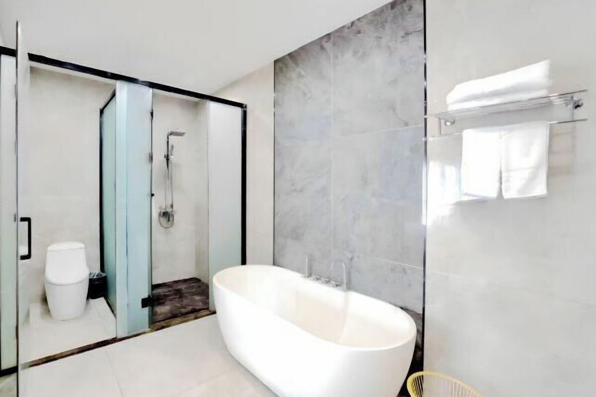 A modern bathroom with a freestanding bathtub, a glass shower enclosure, and a marble wall.
