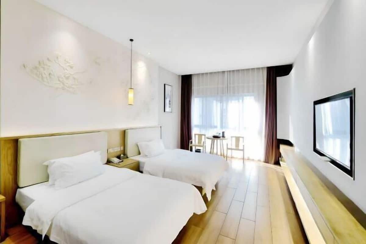 Habitación de hotel con dos camas, televisión, escritorio y ventana con cortinas.